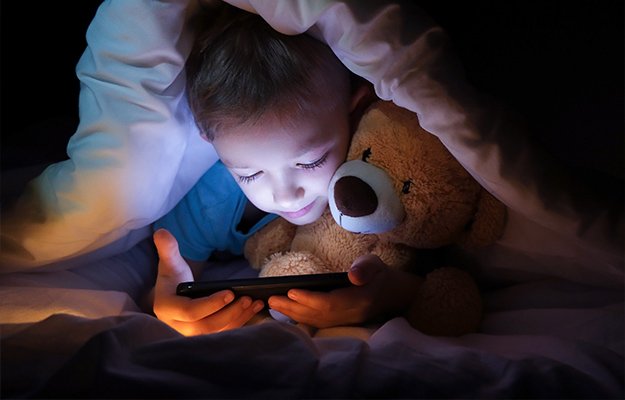 boy-lies-with-toy-bear-in-bed-under-a-blanket-How-Blue-Light-May-Help-with-Health-as-body